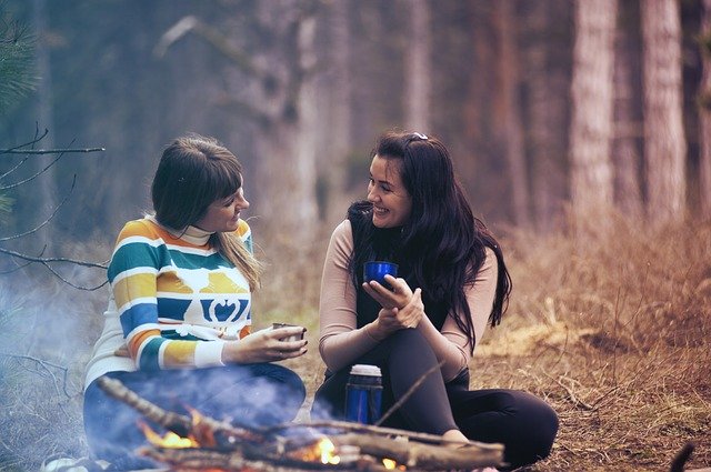two women sitting by campfire talking